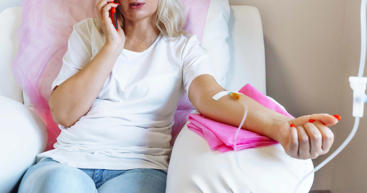 A woman sitting in a comfortable chair receiving IV therapy in Forest Hills, NY while talking on the phone, showing a relaxed and calm wellness treatment setting.